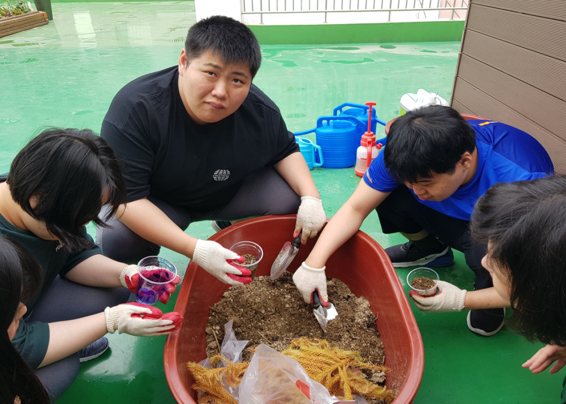 주간보호센터 이용자들이 화분을 만들기 위해 삽을 이용하여 흙을 담고 있는 사진
