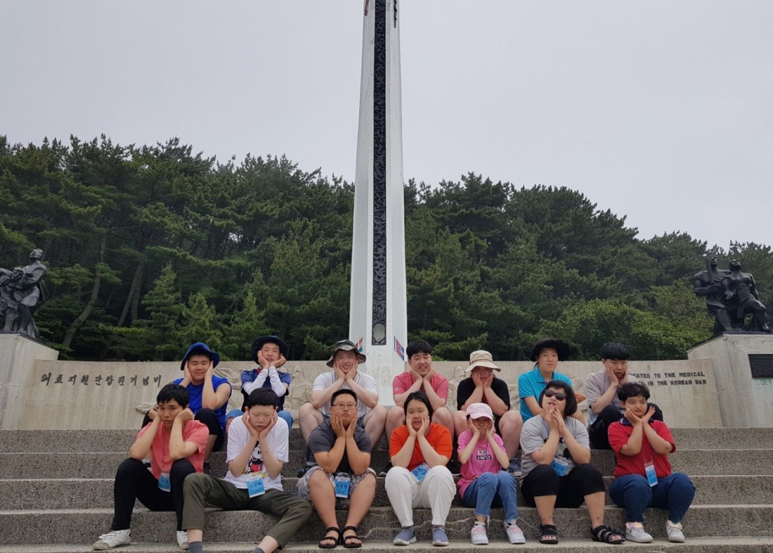 주간보호센터 이용자들이 기념비 앞에 앉아 꽃받침 포즈를 하고 찍은 단체사진