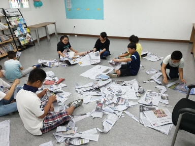 아이들이 바닥에 앉아 신문지를 찢어 공을 만들고 있는 모습