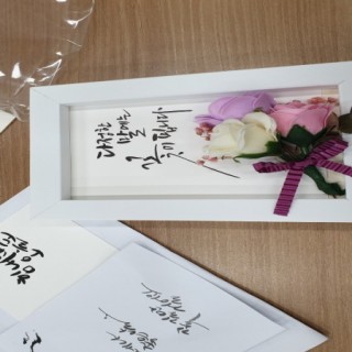 낭만공예교실 참여자가 만든 캘리그라피 액자 다정한 말에는 꽃이 핍니다라는 문구아래 흰색 분홍색 보라색 장미 모형이 붙어있는 사진