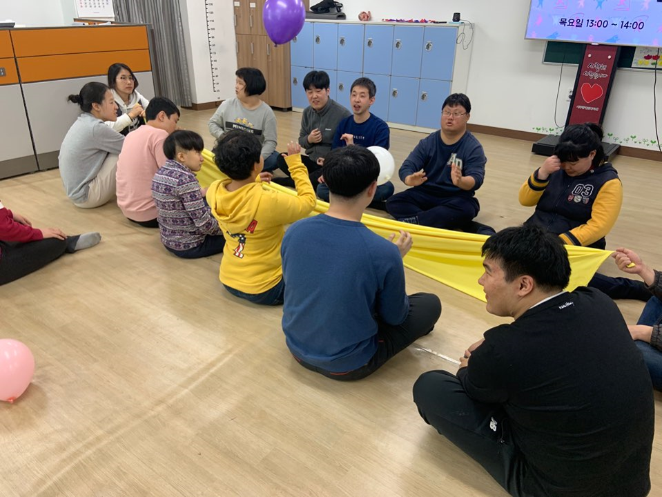 주간보호센터 이용자들이 일렬로 앉아 천을 이용하여 공을 옮기고 있는 모습