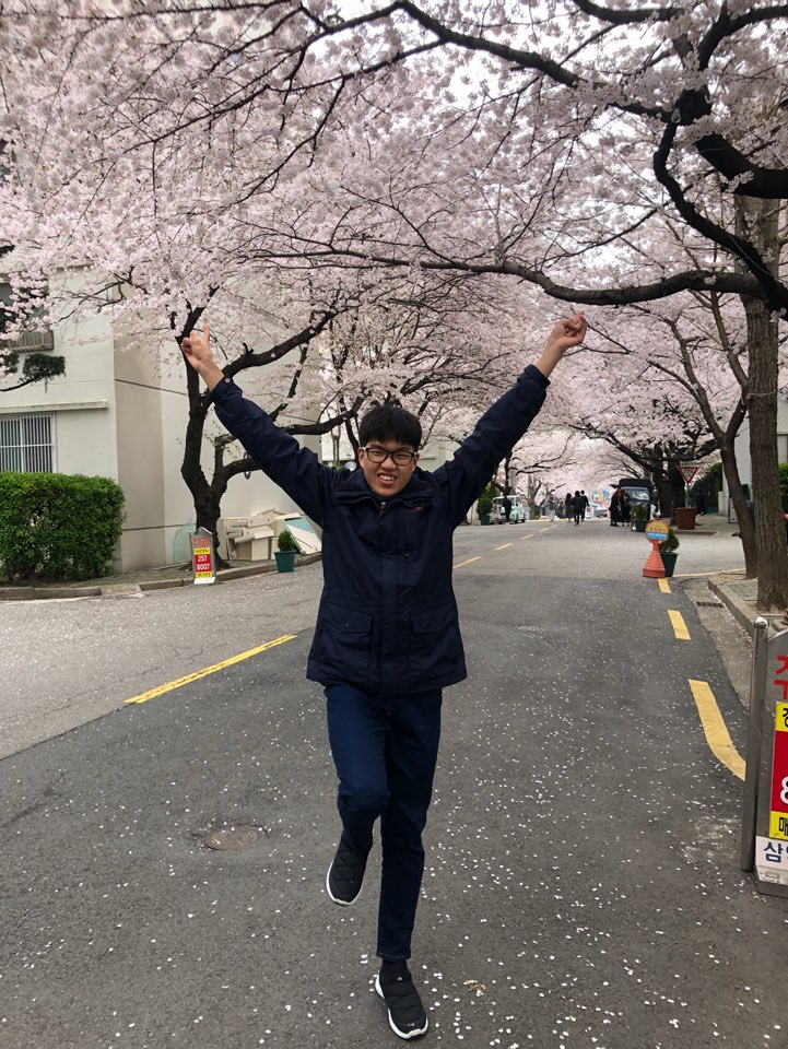 훈련생이 벚꽃이 핀 거리에서 두팔을 위로 들어올리고 즐거워 하는 모습