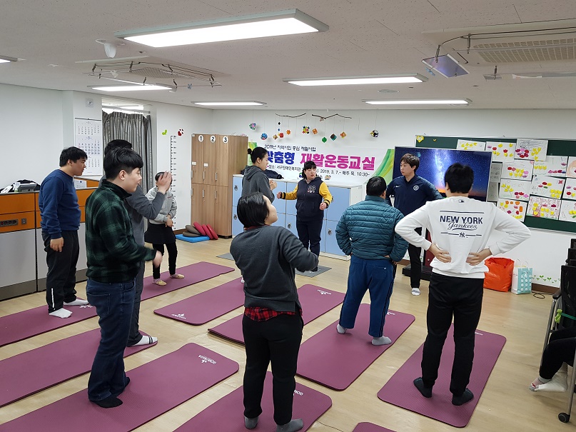 주간보호센터 이용자들이 요가매트위에 서서 강사를 바라보고 있는 모습