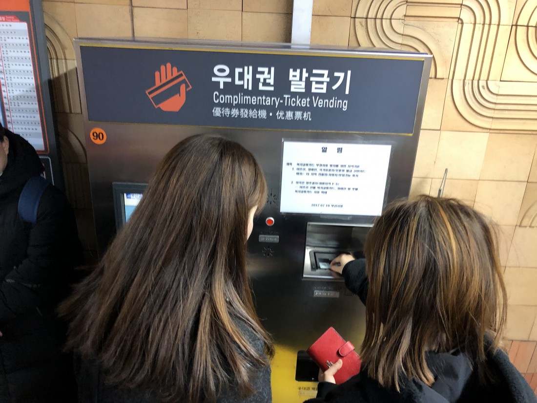 직업적응훈련반 훈련생이 지하철역에 위치한 우대권 발급기 사용에 대해 담당선생님에게 설명을 듣고 있는 모습
