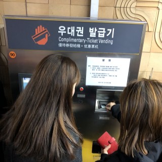 직업적응훈련반 훈련생이 지하철역에 위치한 우대권 발급기 사용에 대해 담당선생님에게 설명을 듣고 있는 모습