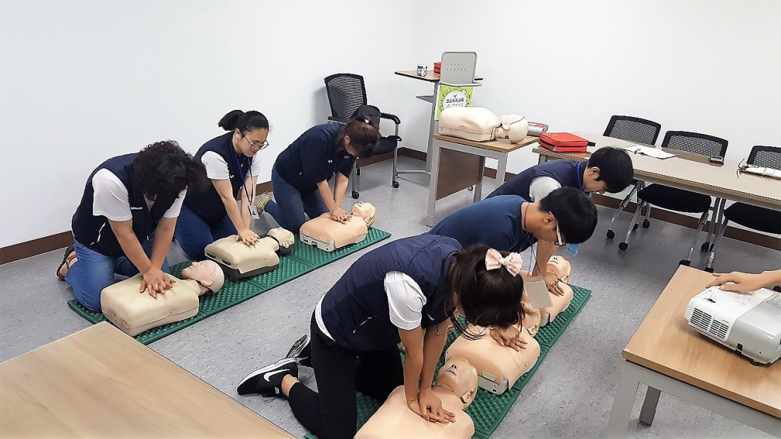 직원들이 모여 심폐소생술 교육을 듣고 직접 체험해보고 있는 사진