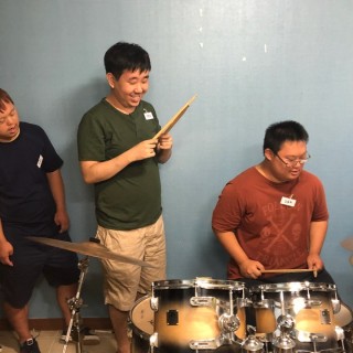 밴드교실에 참여한 이용자가 드럼스틱을 들고 밝게 웃고 있는 모습
