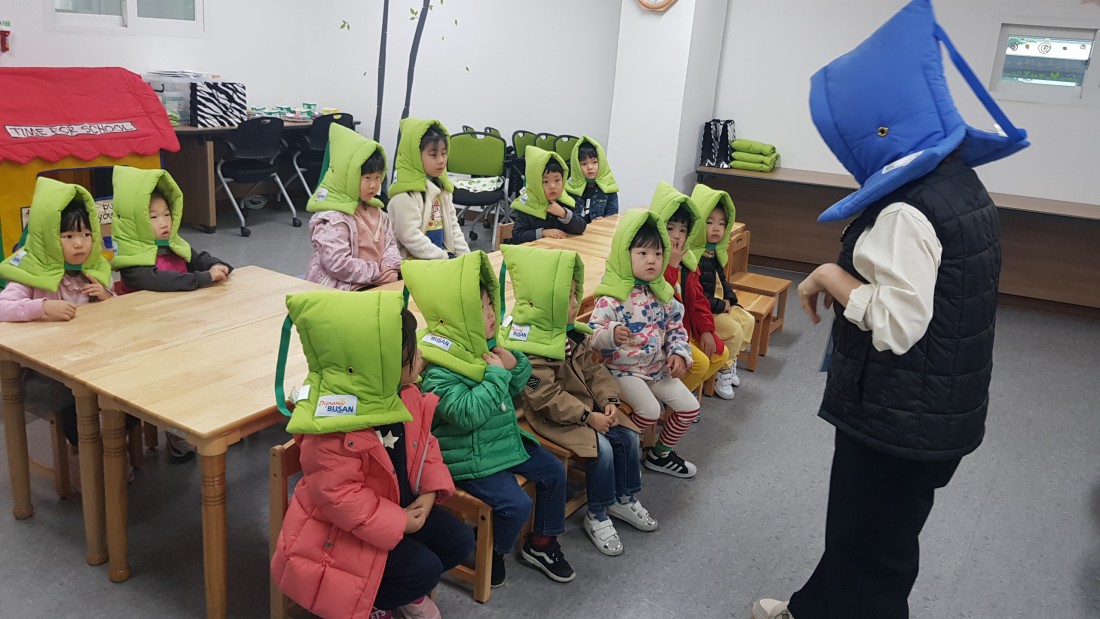 강사와 아이들이 머리에 방재모자를 뒤집어쓰고 지진에 대비한 교육을 진행하고 있는 사진